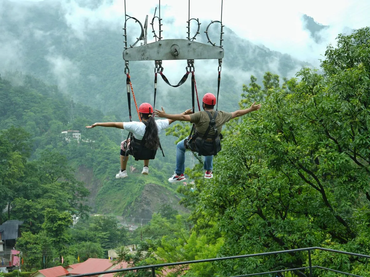 Two people on a giant swing above green hills in Dandeli
