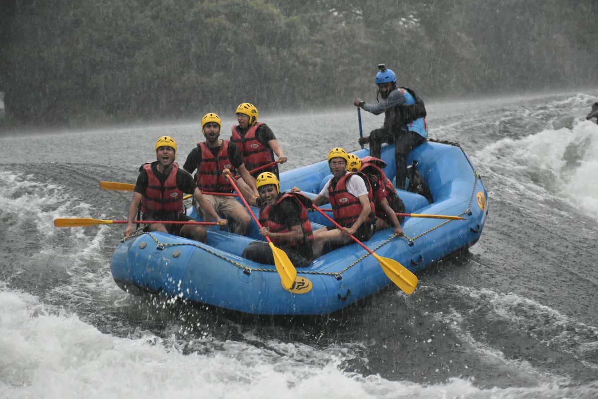 Guide and rafters in a blue raft paddling through Kali River rapids